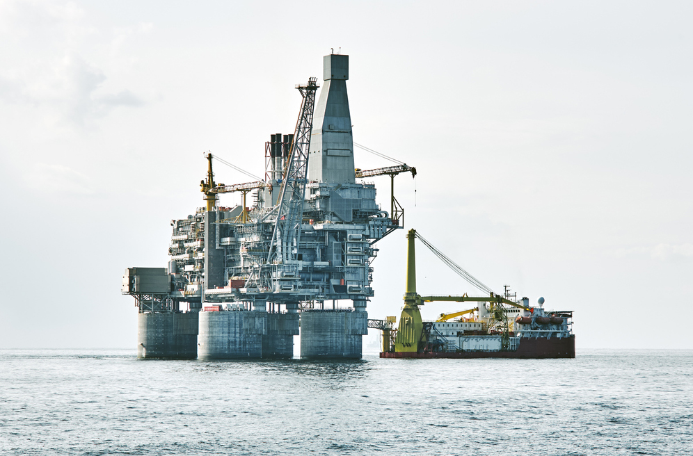 Oil rig silhouette and support vessel on offshore area. Gray cloudy sky, sea wave